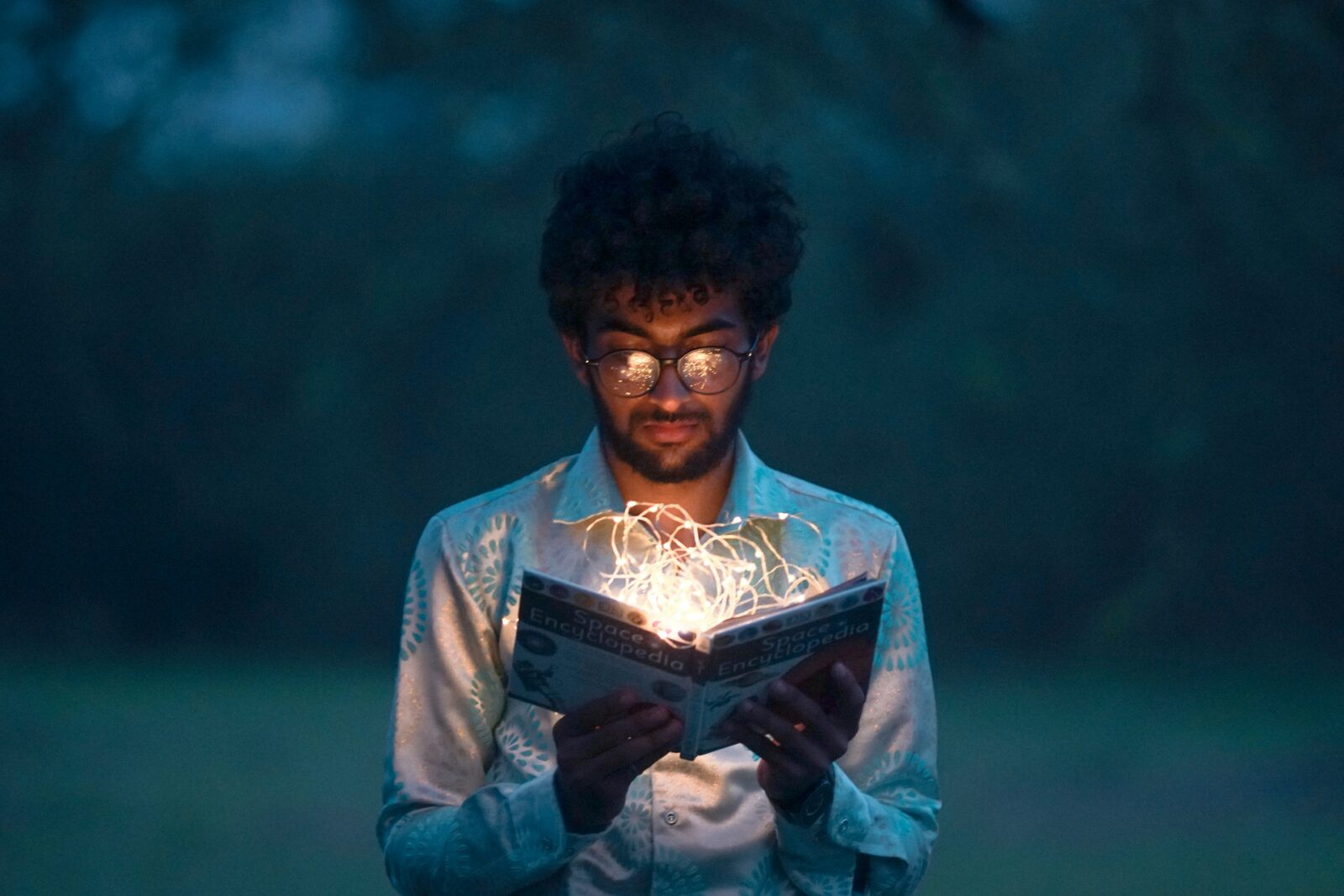 an Asian man looking into a book with sparks coming out of it