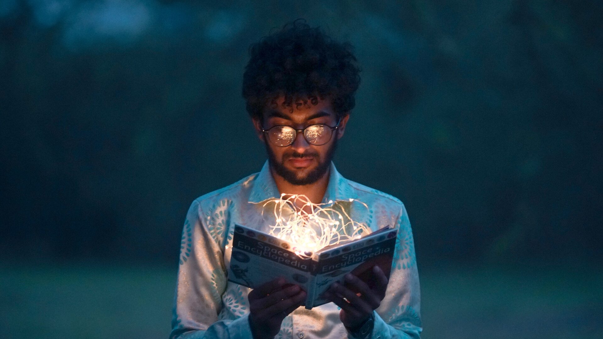 an Asian man looking into a book with sparks coming out of it