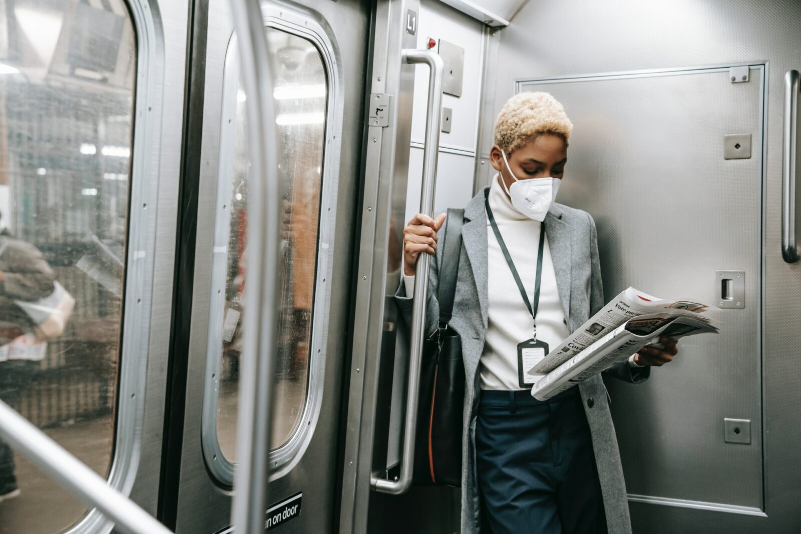 Black woman wearing a medical mask reading a newspaper inside a subway train