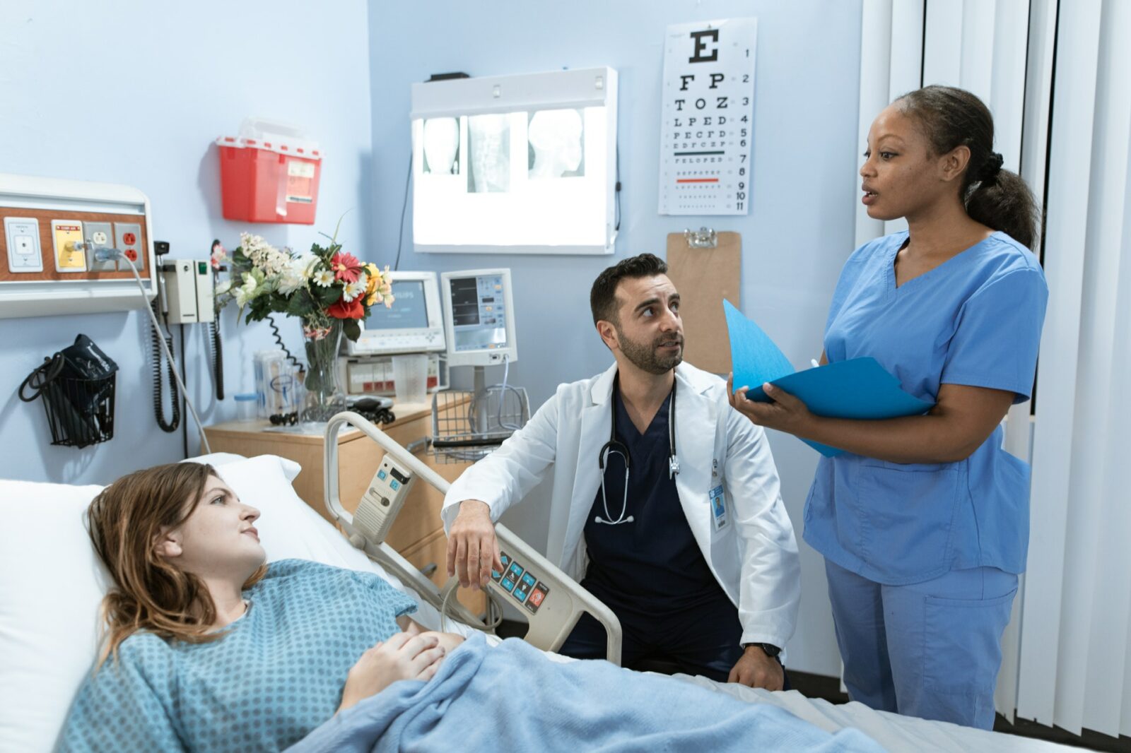 black woman nurse consulting with a white woman patient and male middle eastern doctor in medical office