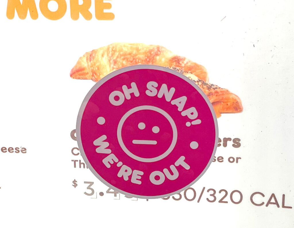 a sticker that says "oh snap! we're out" stuck on a menu board covering a menu item