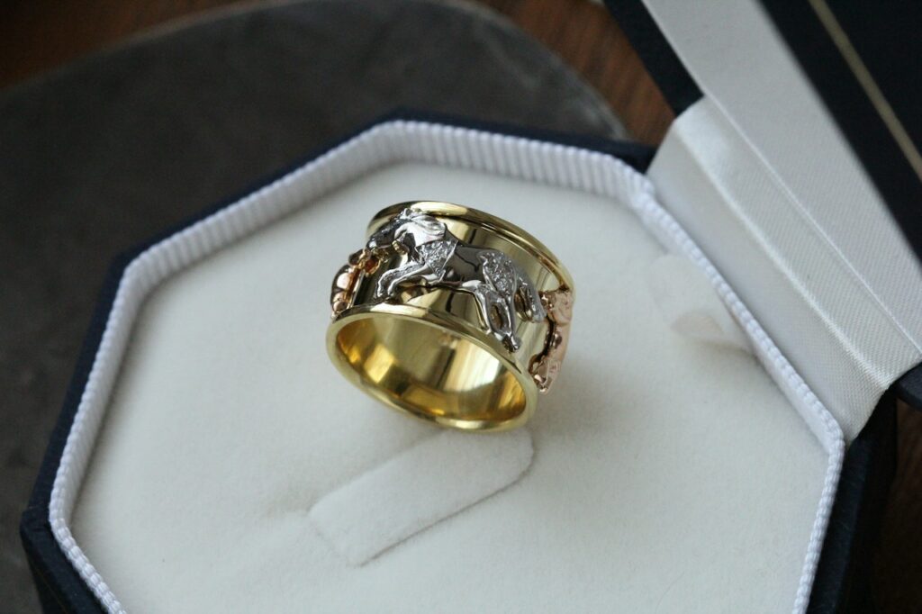 a thick gold ring with horses on it sitting on a jewelry box