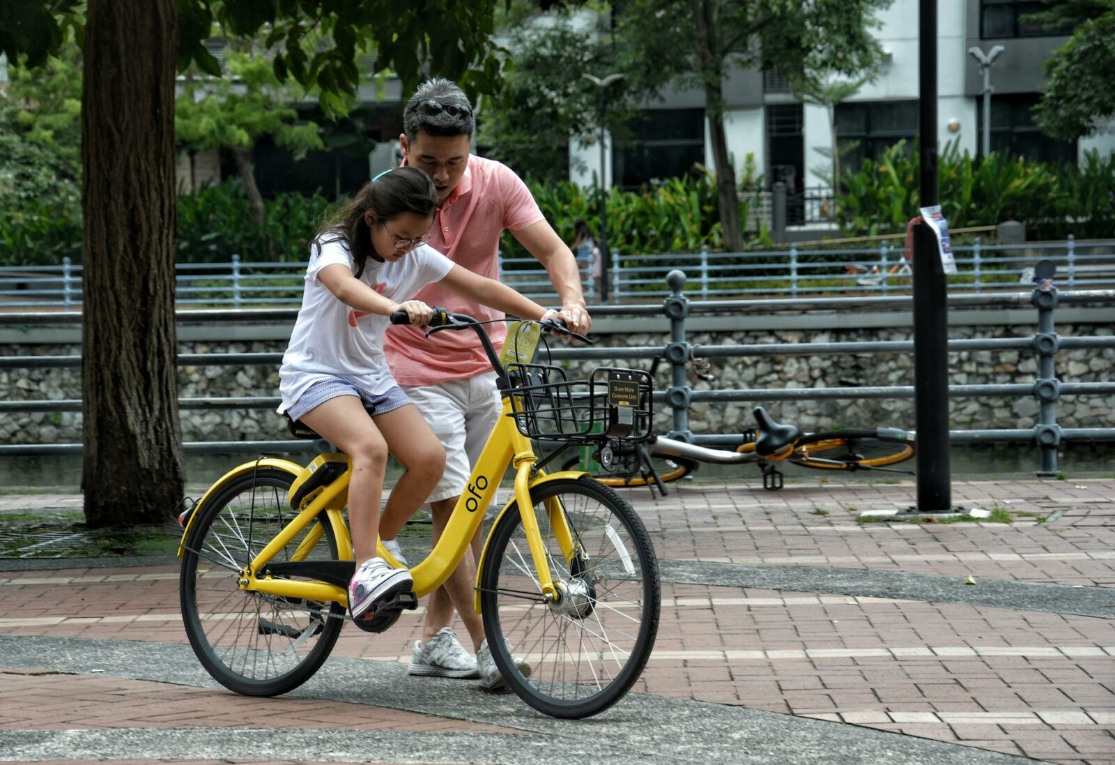 an Asian man helping a girl learn to ride a bike