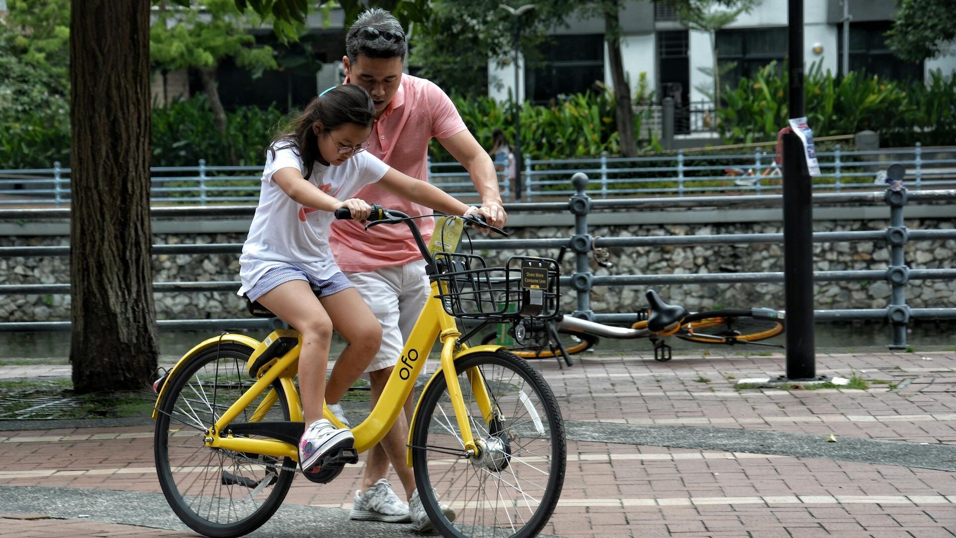 an Asian man helping a girl learn to ride a bike
