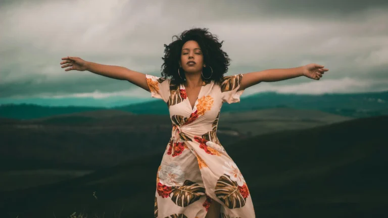 a black woman standing in a powerful pose with arms wide and mountains behind her